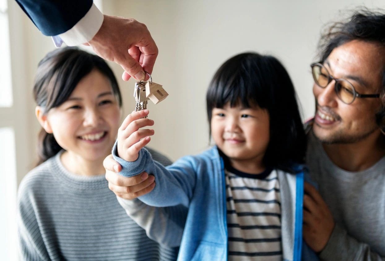 A young girl receives house keys from an adult while her smiling parents look on.