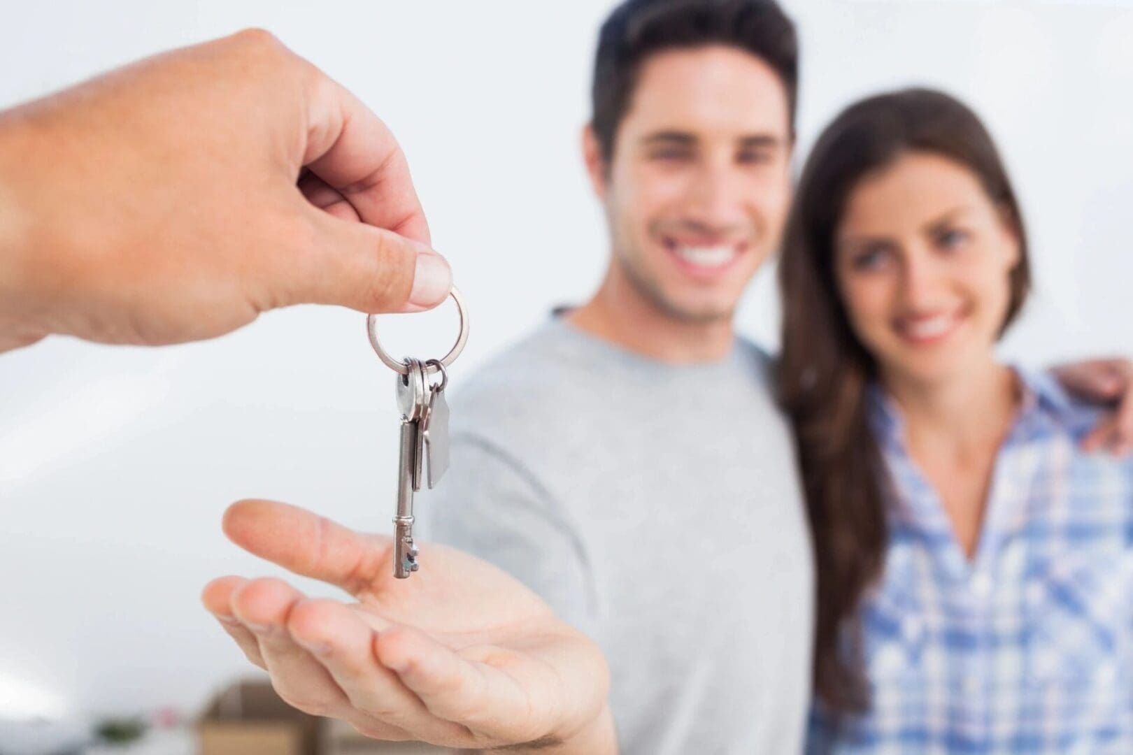 A person hands over keys to a smiling couple, with the focus on the keys in the foreground.